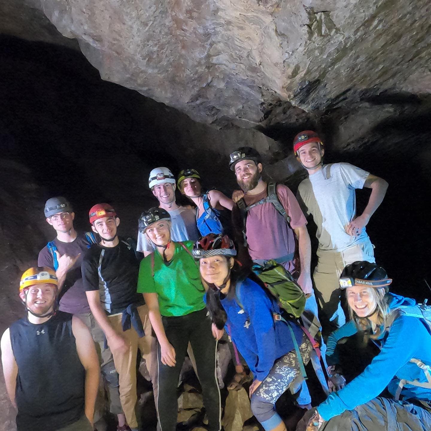 Eleven people in headlamps and helmets smiling together inside a dark cave